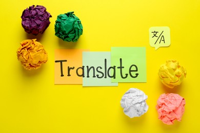 Word Translate made with sticky notes near crumpled paper balls on yellow background, flat lay