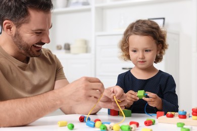 Motor skills development. Father and daughter playing with wooden pieces and strings for threading activity at table indoors