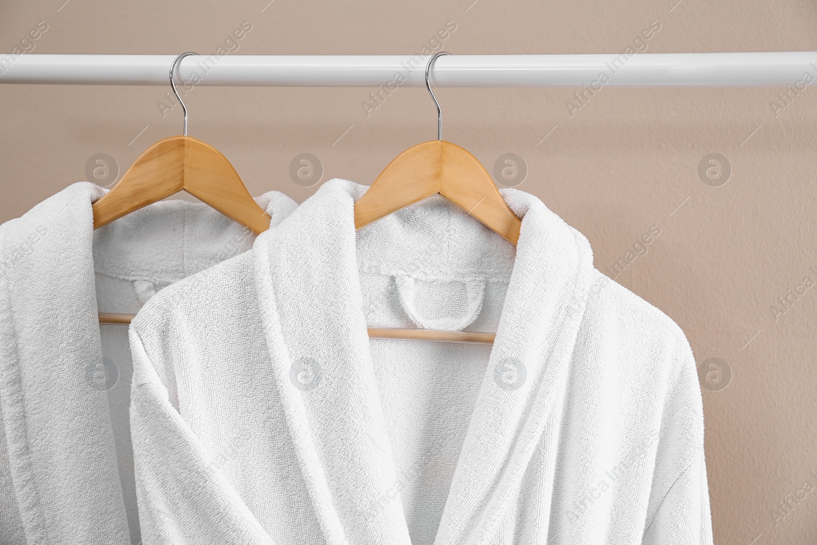 Photo of Fresh white bathrobes hanging on rack near beige wall