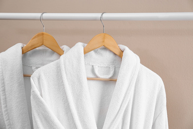 Fresh white bathrobes hanging on rack near beige wall