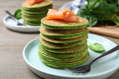 Tasty spinach pancakes with salmon on wooden table, closeup