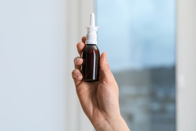 Photo of Woman holding nasal spray bottle indoors, closeup