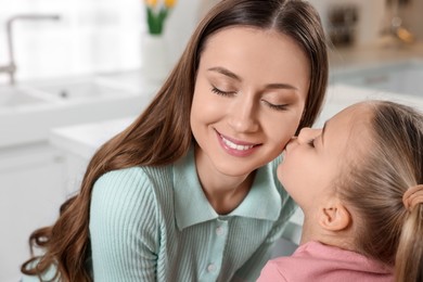 Photo of Cute daughter kissing her mom in kitchen