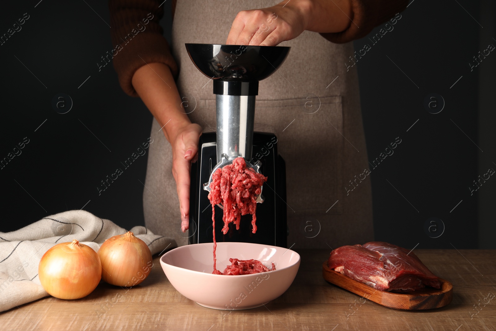 Photo of Woman making beef mince with electric meat grinder at wooden table, closeup