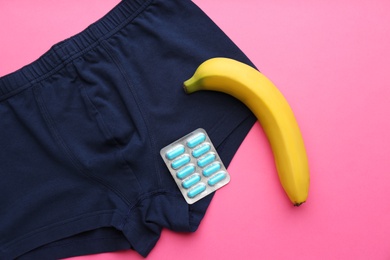 Photo of Men's underwear, pills and banana on pink background, flat lay. Potency problem concept