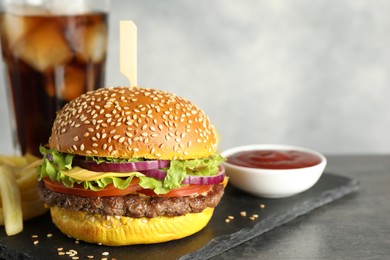 Photo of Burger with delicious patty, soda drink, french fries and sauce on dark table against gray background, closeup