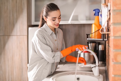 Photo of Young woman cleaning tap in kitchen