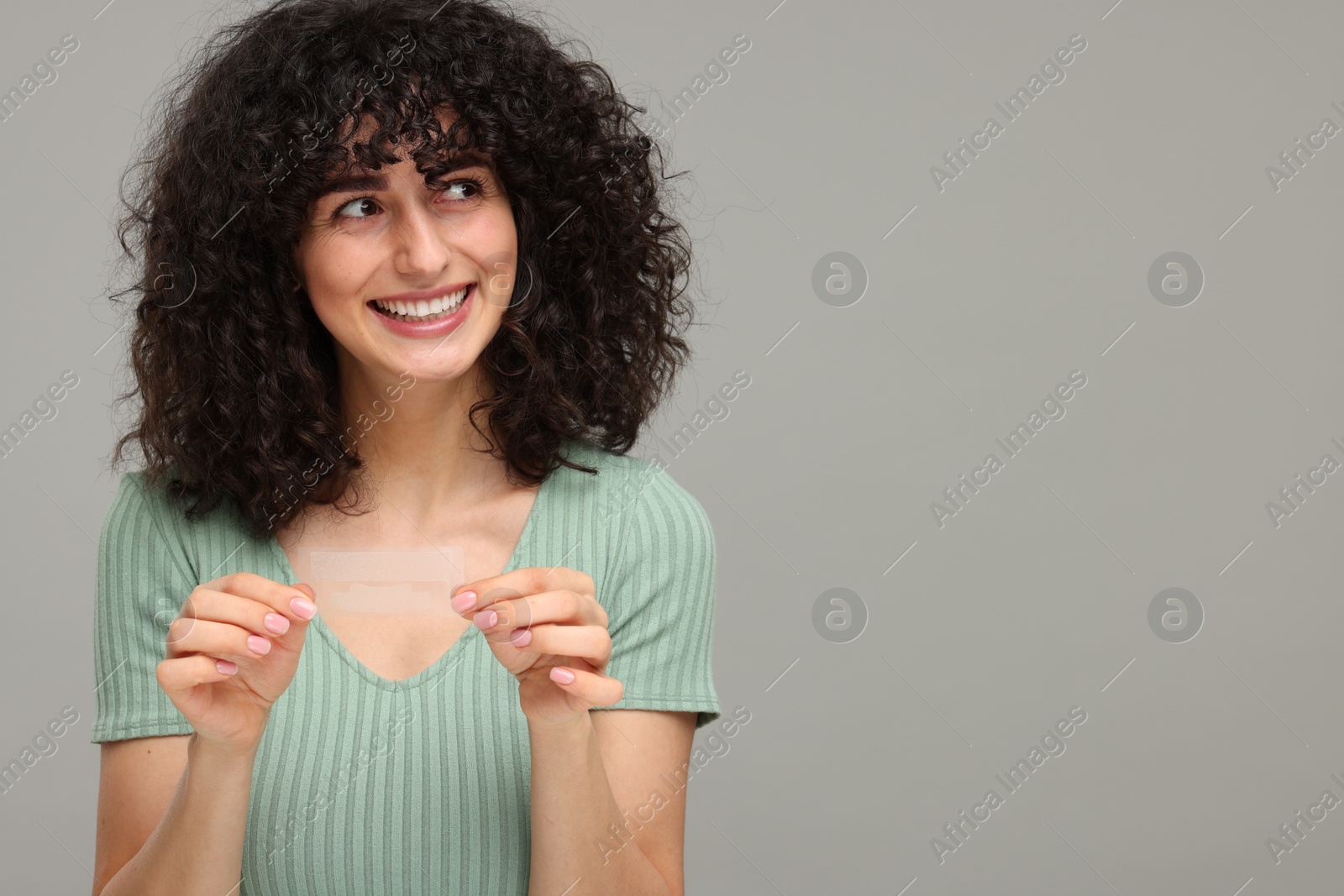 Photo of Young woman holding teeth whitening strips on grey background, space for text