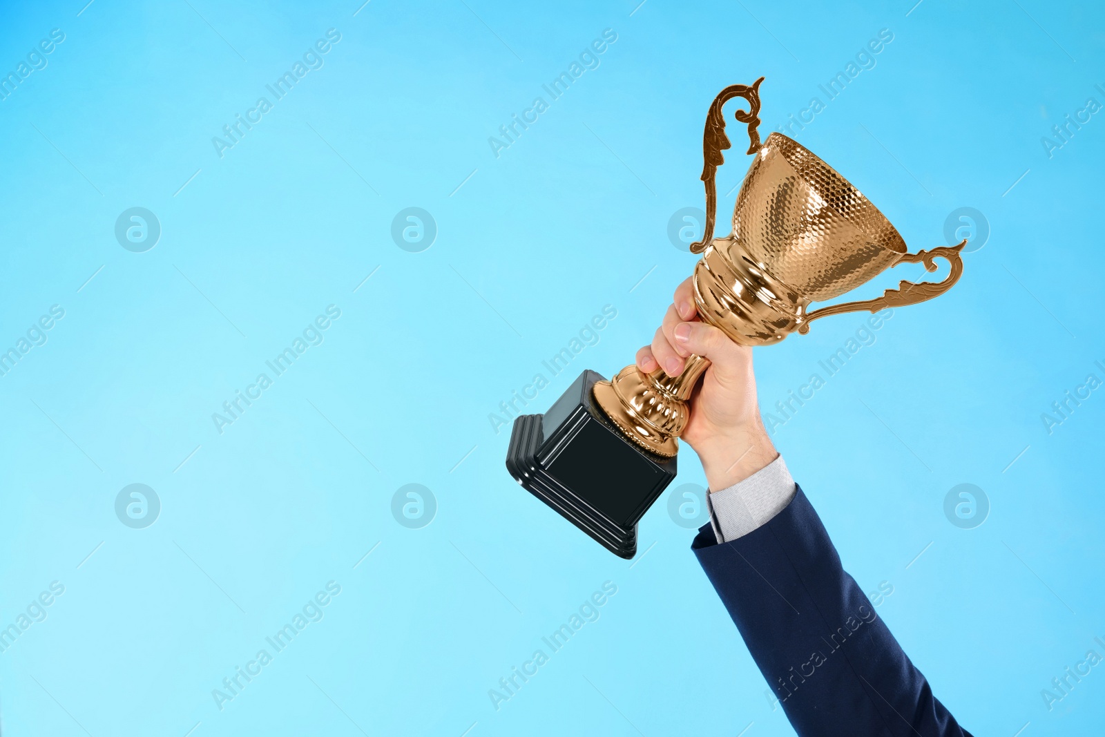 Photo of Businessman holding gold trophy cup on light blue background, closeup. Space for text