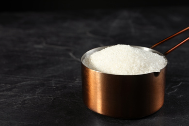 Metal measuring scoop of granulated sugar on black table