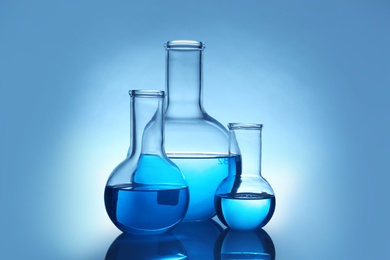 Photo of Flasks with liquid on table against color background. Laboratory analysis