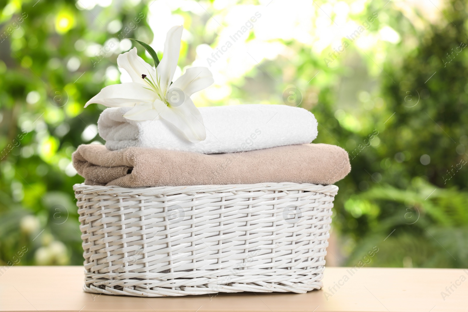Photo of Basket with soft bath towels and flower on table against blurred background