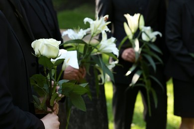 Photo of People with flowers outdoors, closeup. Funeral ceremony