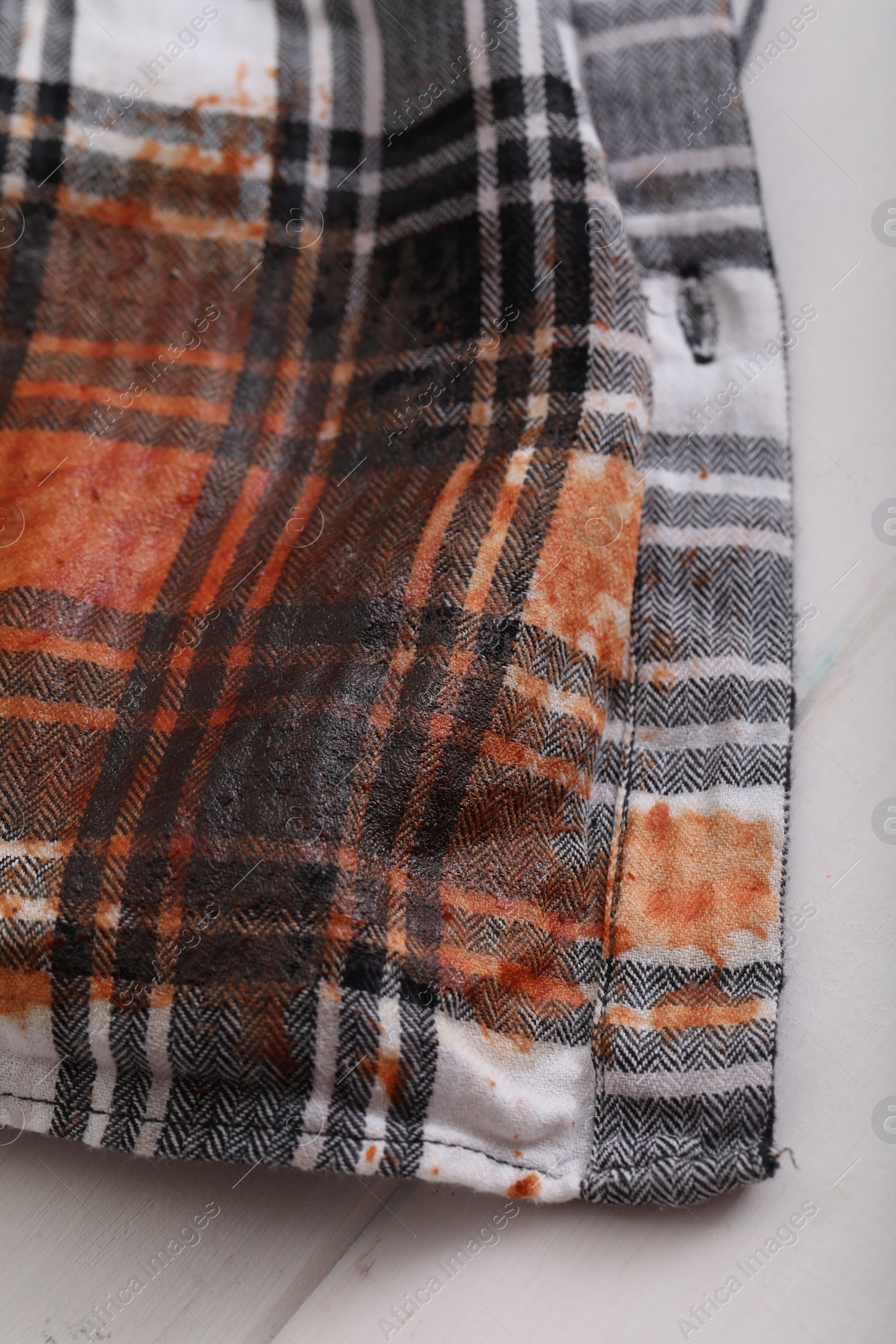 Photo of Shirt with stain of sauce on white wooden table, closeup