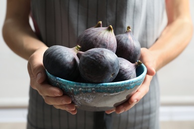 Photo of Woman holding bowl with fresh ripe figs on light background