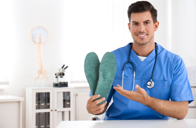 Photo of Handsome male orthopedist showing insoles in clinic