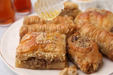 Photo of Eastern sweets. Pouring honey onto pieces of tasty baklava on table, closeup