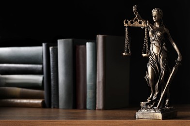 Photo of Statue of Lady Justice near books on wooden table, space for text. Symbol of fair treatment under law