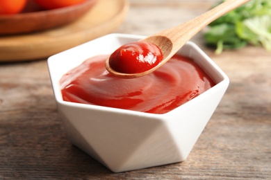 Photo of Spoon and bowl with homemade tomato sauce on wooden table