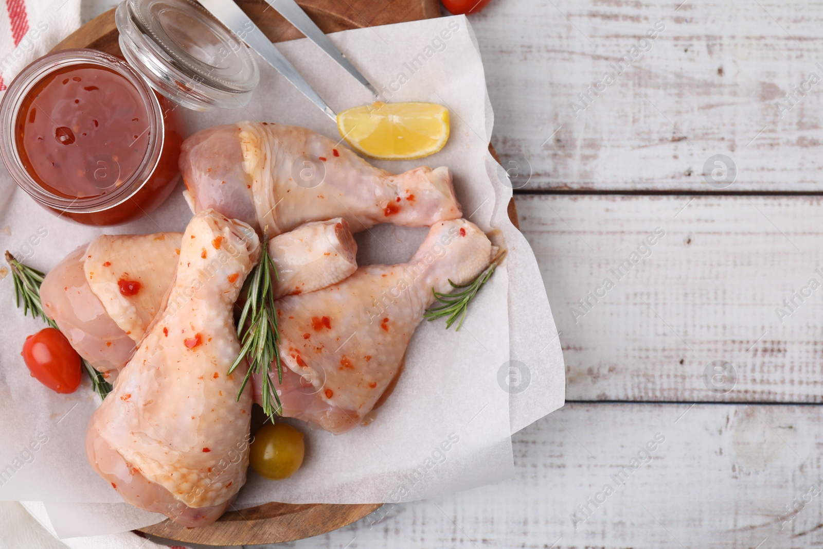 Photo of Marinade, raw chicken drumsticks, tomatoes and rosemary on white wooden table, flat lay. Space for text