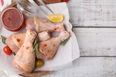 Marinade, raw chicken drumsticks, tomatoes and rosemary on white wooden table, flat lay. Space for text