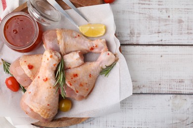 Photo of Marinade, raw chicken drumsticks, tomatoes and rosemary on white wooden table, flat lay. Space for text