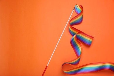 Photo of Stick with rainbow ribbon on orange background, top view and space for text. LGBT pride