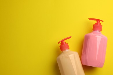 Bottles of liquid soap on yellow background, flat lay. Space for text