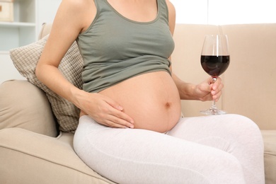 Photo of Pregnant woman with glass of red wine at home. Alcohol addiction