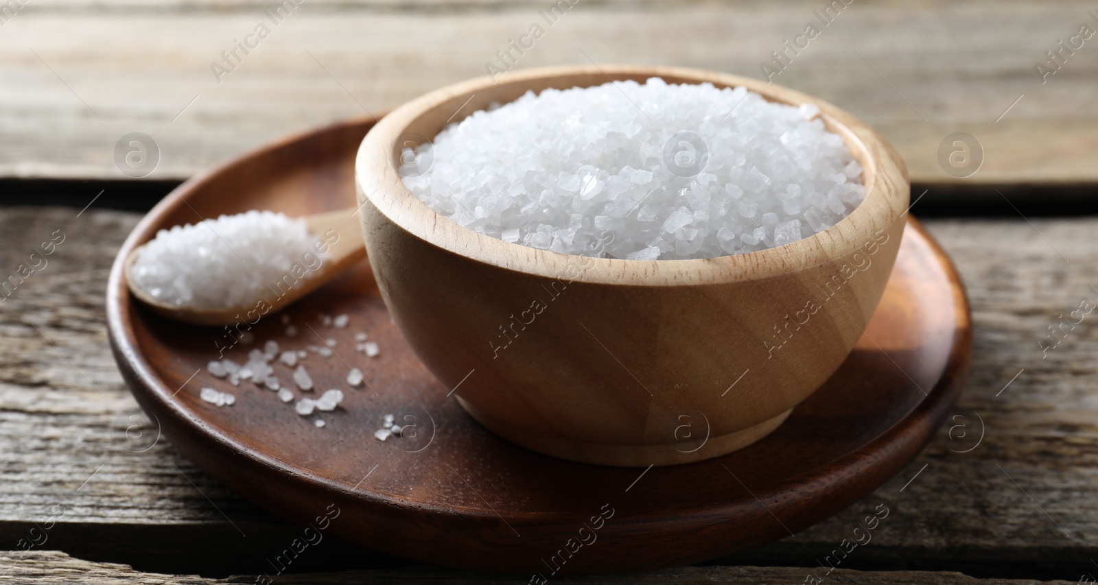 Photo of Organic salt in bowl and spoon on wooden table, closeup