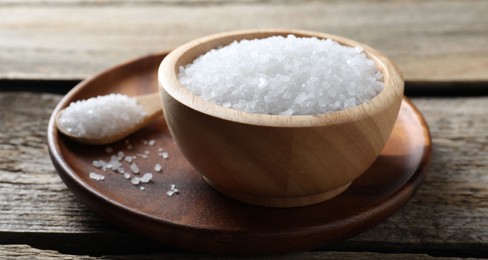 Photo of Organic salt in bowl and spoon on wooden table, closeup