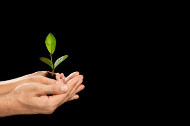 Man and his child holding soil with green plant in hands on black background. Family concept