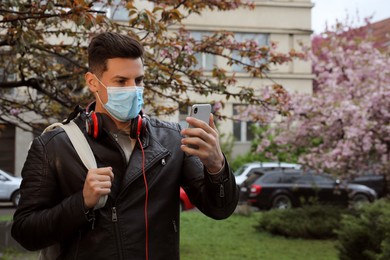 Photo of Tourist in medical mask with smartphone on city street