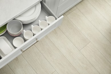 Clean plates, bowls, butter dish and cups in drawer indoors, top view. Space for text