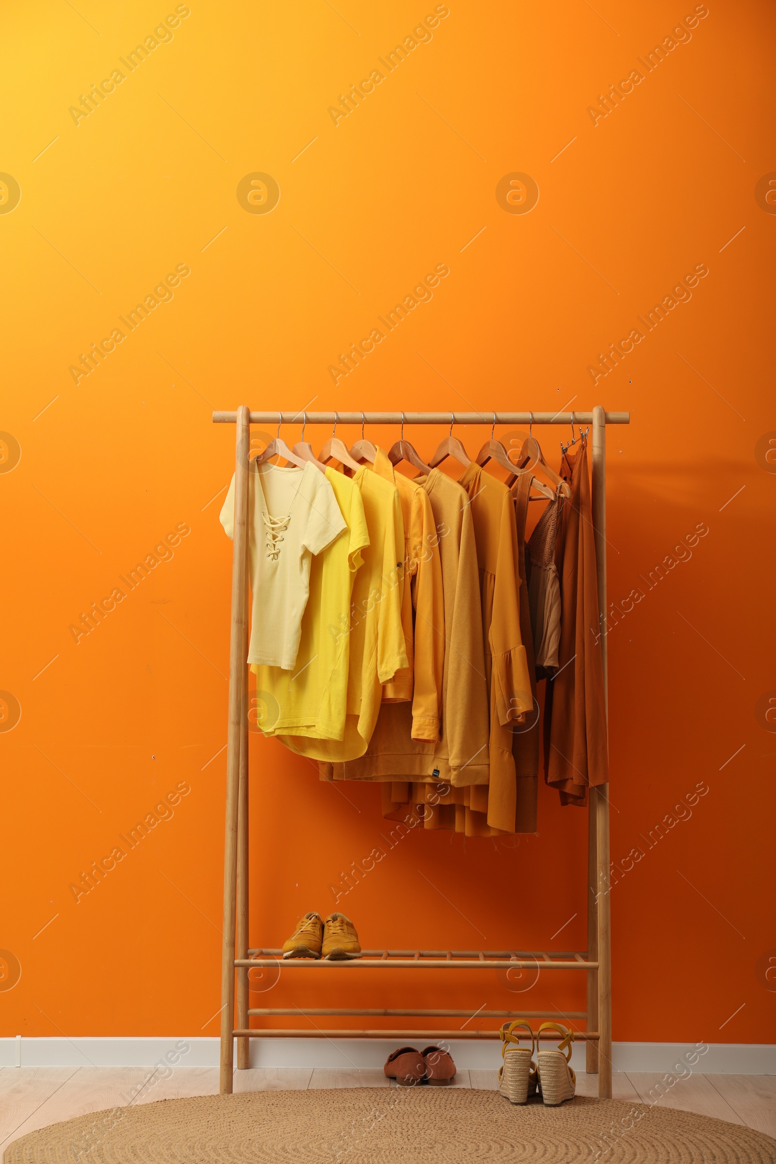 Photo of Rack with different stylish women`s clothes and shoes near orange wall indoors