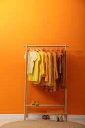 Rack with different stylish women`s clothes and shoes near orange wall indoors