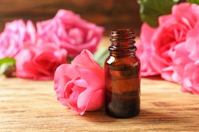 Photo of Bottle of rose essential oil and flowers on wooden table