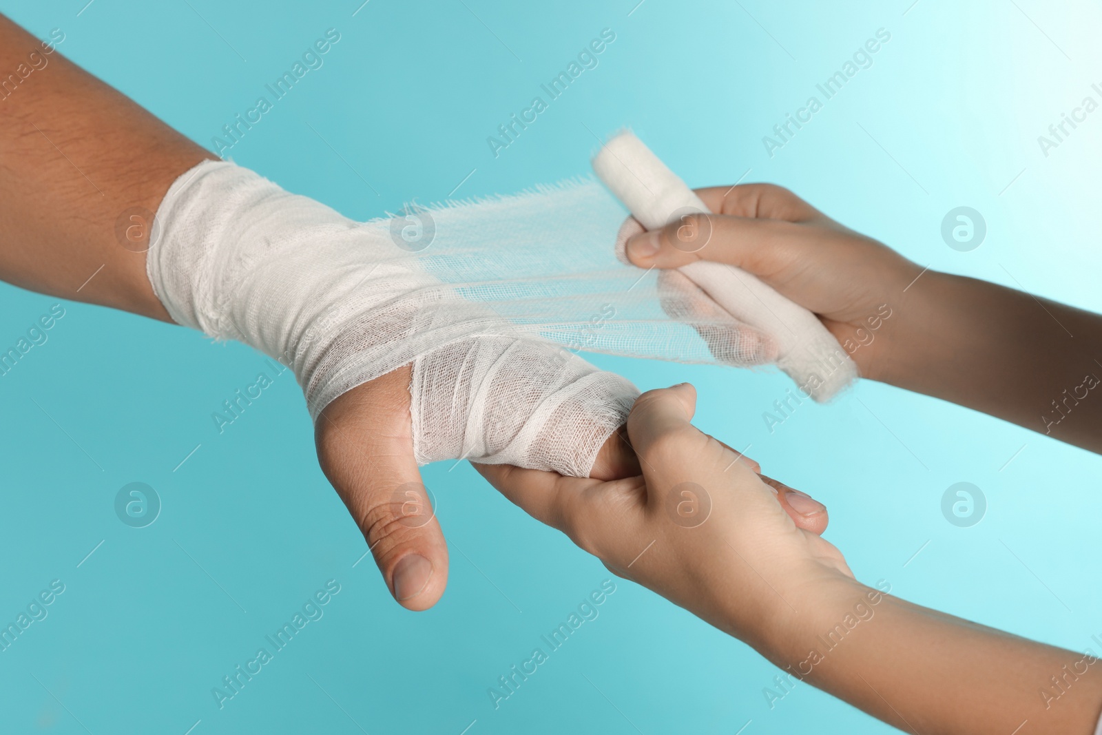 Photo of Doctor applying bandage onto patient's hand on light blue background, closeup