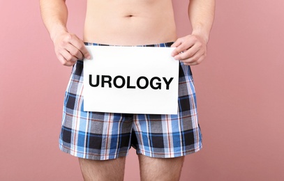 Photo of Young man holding paper with word UROLOGY on color background