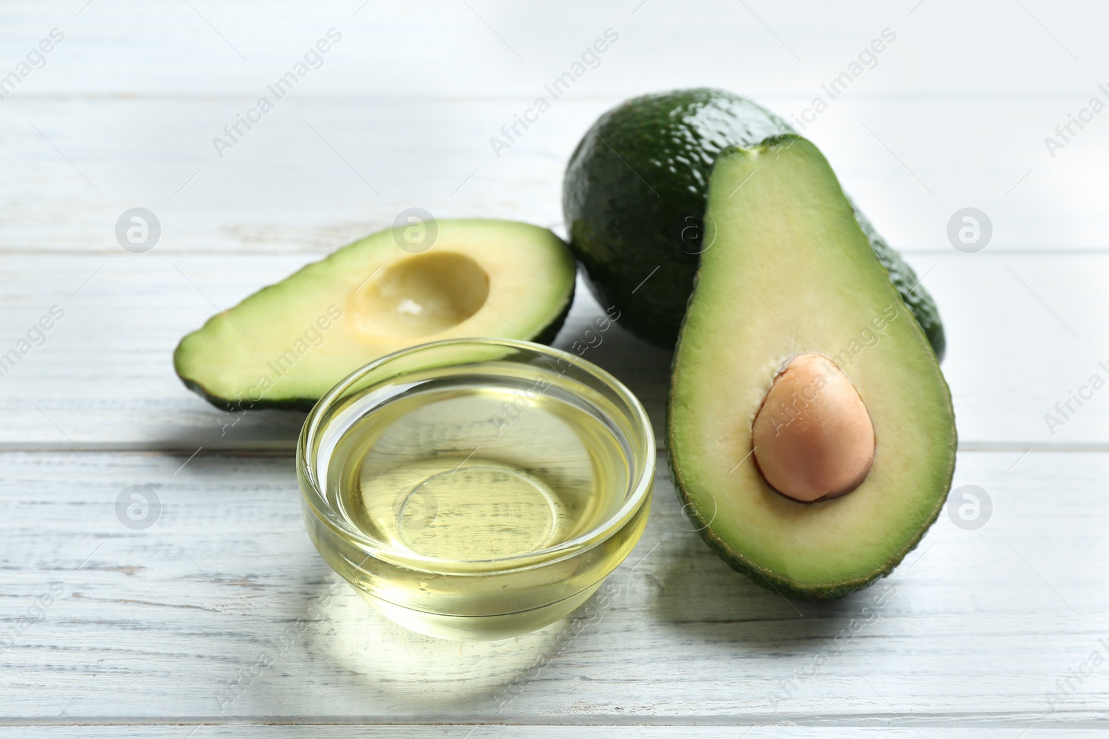 Photo of Bowl of natural oil and avocados on white wooden background