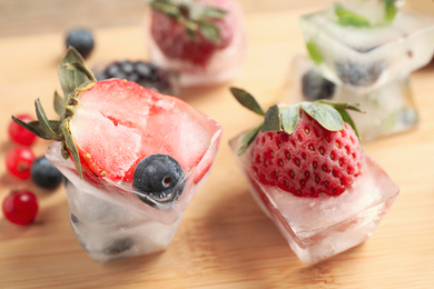 Ice cubes with different berries and mint on wooden board, closeup