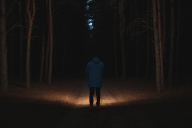 Photo of Man with bright flashlight in forest at night