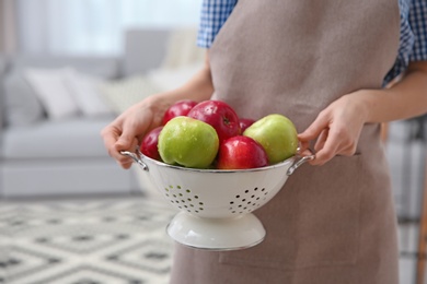 Photo of Woman holding colander with ripe apples on blurred background