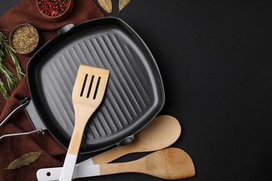 Wooden kitchen utensils, frying pan and spices on black table, flat lay. Space for text