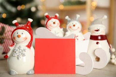 Decorative snowmen near blank red card on table, space for text