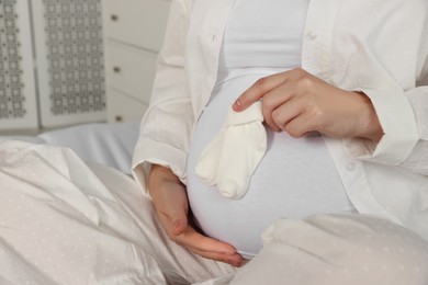 Photo of Pregnant woman with baby socks on bed at home, closeup