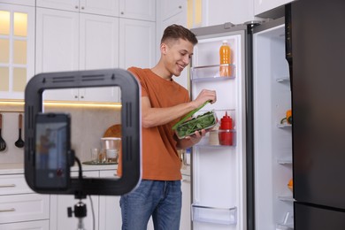 Smiling food blogger opening container with spinach while recording video in kitchen