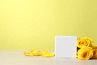 Photo of Beautiful presentation for product. White square podium and roses on wooden table against yellow background, space for text