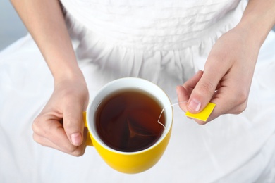 Photo of Woman taking tea bag out of cup with beverage, closeup