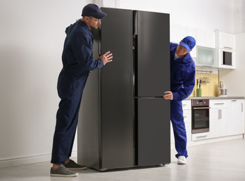 Professional workers carrying modern refrigerator in kitchen